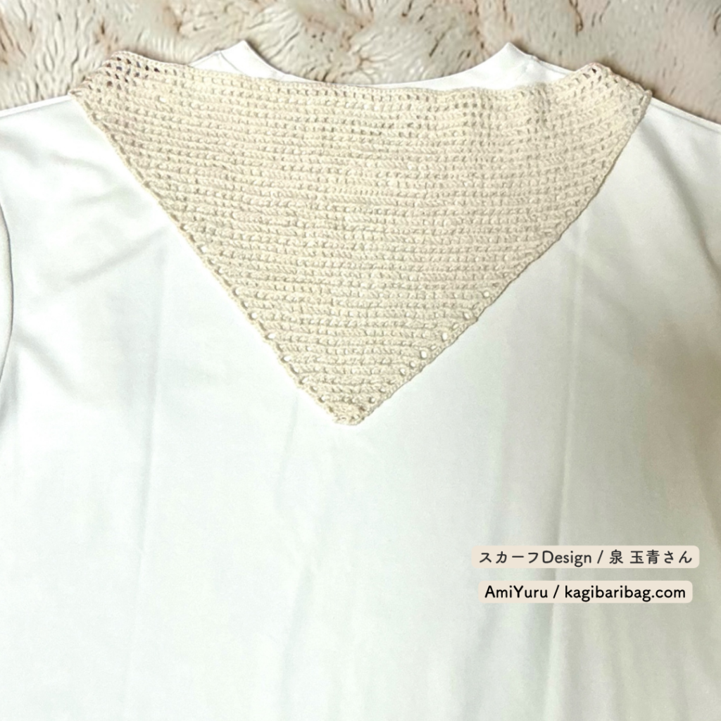 ウール糸を使って、かぎ針で編む方眼編みの三角スカーフを白色の服と合わせた画像。